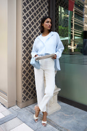 Woman in light blue jacket and white pants standing on a city street.
